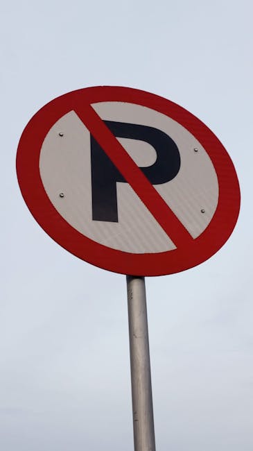 A circular street sign with a white background, featuring a bold black letter 'P' crossed out by a red diagonal line, indicating no parking. The sign is mounted on a grey metal pole positioned against an overcast sky. This type of sign is relevant in the context of house removals and relocation services, such as those offered by Lambeth Man and Van, as it highlights parking restrictions that may affect loading and unloading during home relocation or furniture transport processes.