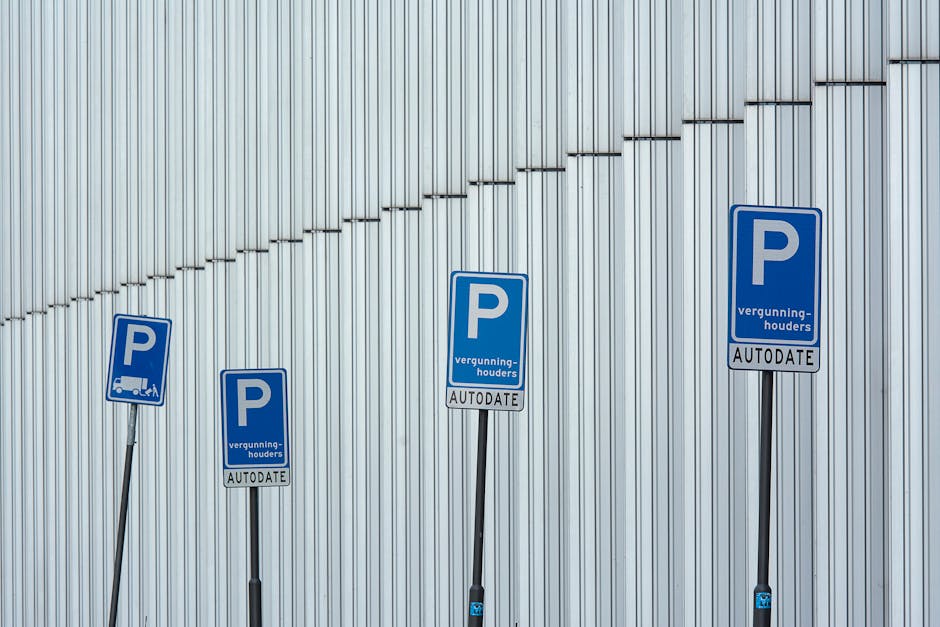 Four parking permit signs mounted on black metal poles in front of a modern, metallic wall with vertical panels. The signs are blue with a white letter 'P' and include additional text indicating parking authorization, including the words 'vergunnings-houders' and 'AUTODATE.' The signs are staggered at different heights along a paved area, suggesting designated parking spots for permit holders, which is relevant to loading or parking logistics during house removals. The overall scene depicts a clean, urban environment with no visible vehicles or furniture, focusing on the parking permit signage that may be pertinent for coordinating street parking during home relocation services provided by Lambeth Man and Van.