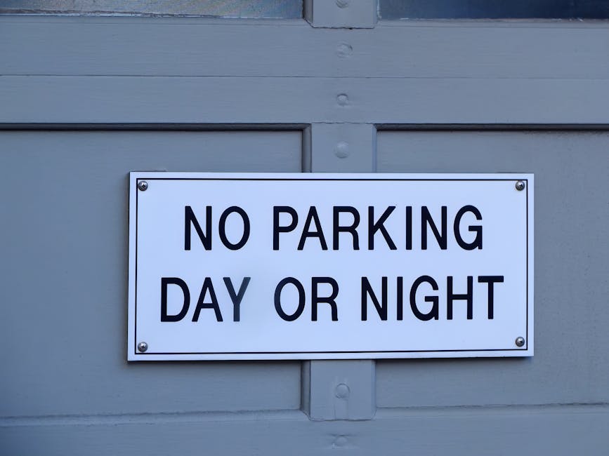 A circular street sign with a white background, featuring a bold black letter 'P' crossed out by a red diagonal line, indicating no parking. The sign is mounted on a grey metal pole positioned against an overcast sky. This type of sign is relevant in the context of house removals and relocation services, such as those offered by Lambeth Man and Van, as it highlights parking restrictions that may affect loading and unloading during home relocation or furniture transport processes.
